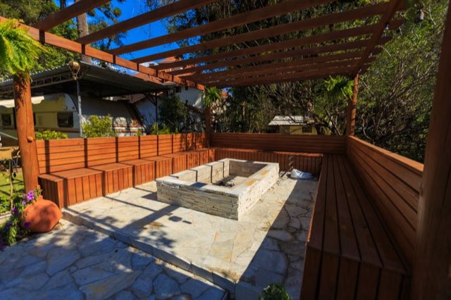 Wooden deck with a pergola and built-in stone fire pit