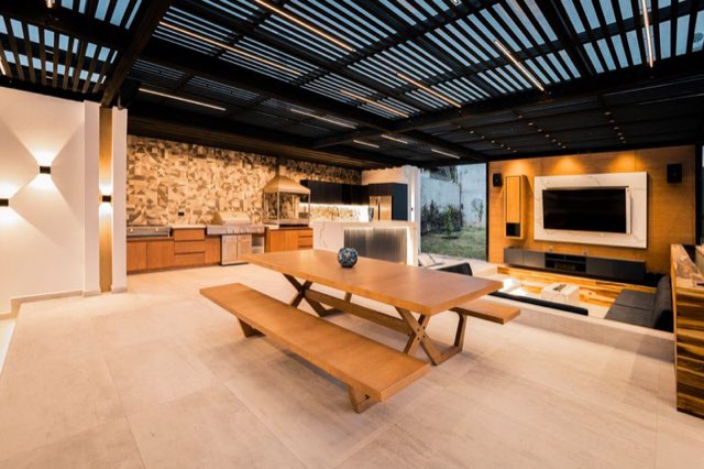 Covered outdoor kitchen and lounge with a stone wall and warm evening light